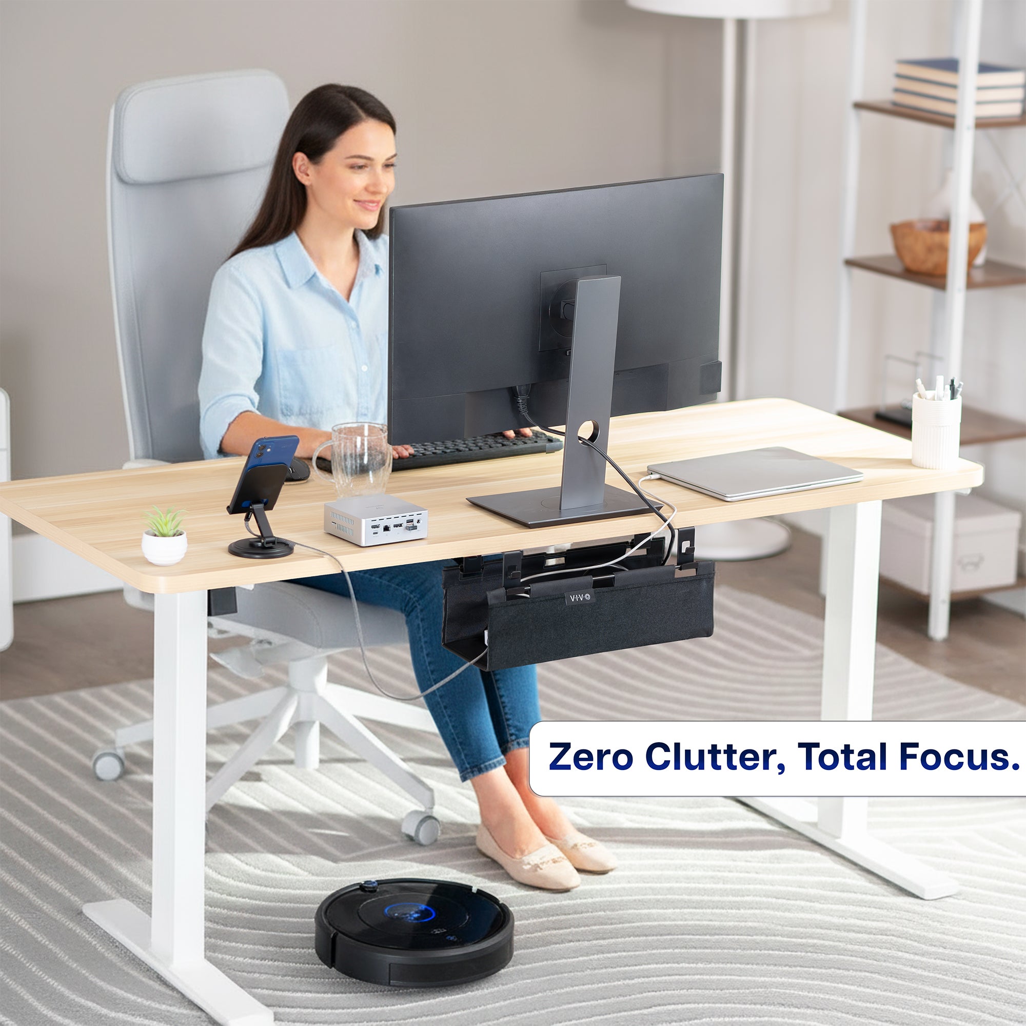 Woman working at a desk with a Under Desk Fabric Cable Management Tray and a robot vacuum cleaner on the floor.
