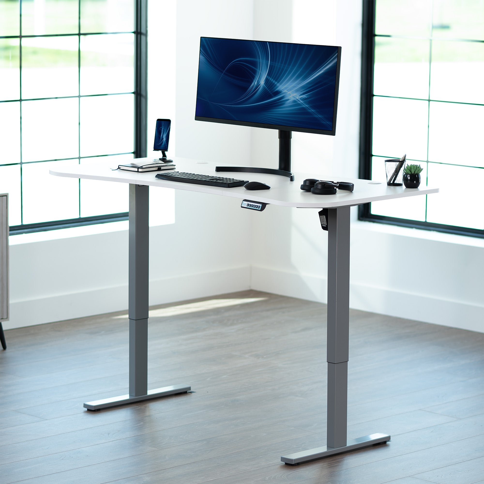 White top grey frame, electric, sit to stand, height adjustable desk in office setting.