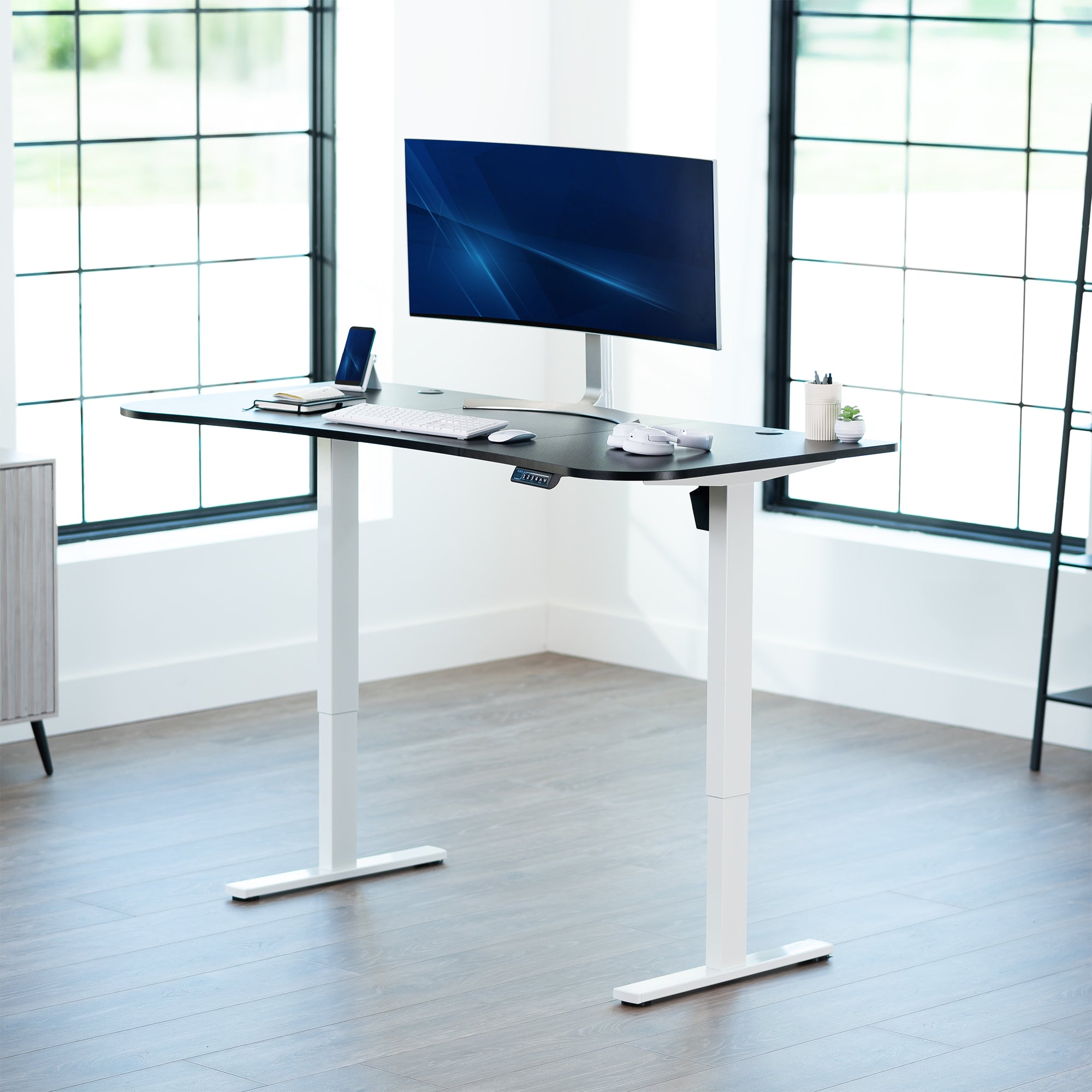 Black top white frame, electric, sit to stand, height adjustable desk in office setting.