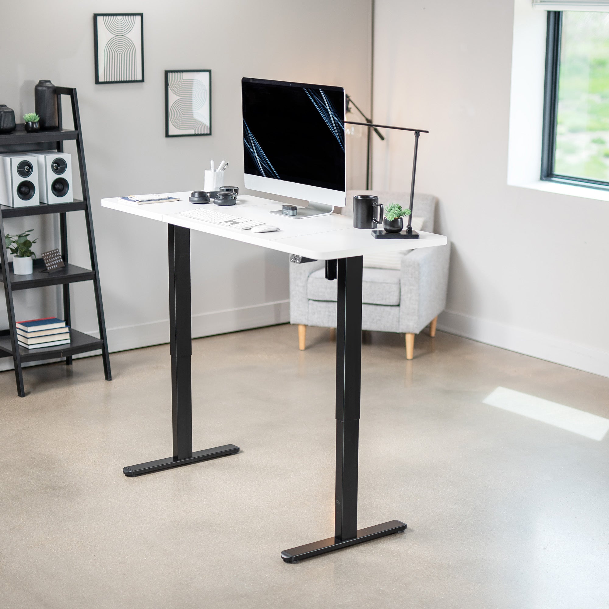White and black adjustable desk in a modern office setting with a computer monitor and office supplies.