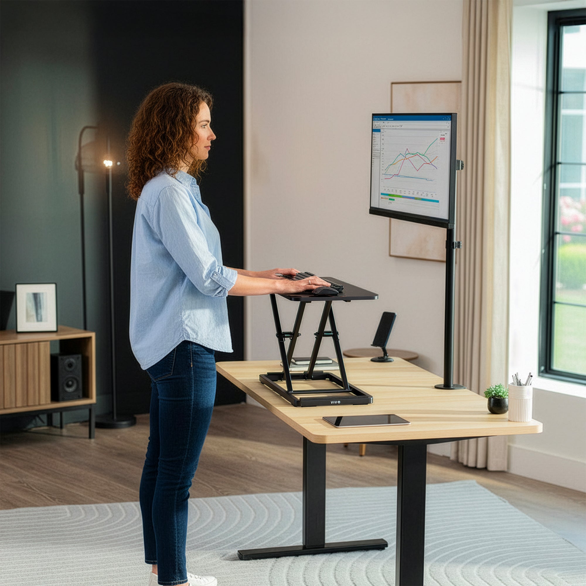 Woman using a standing desk with a monitor in a home office setting