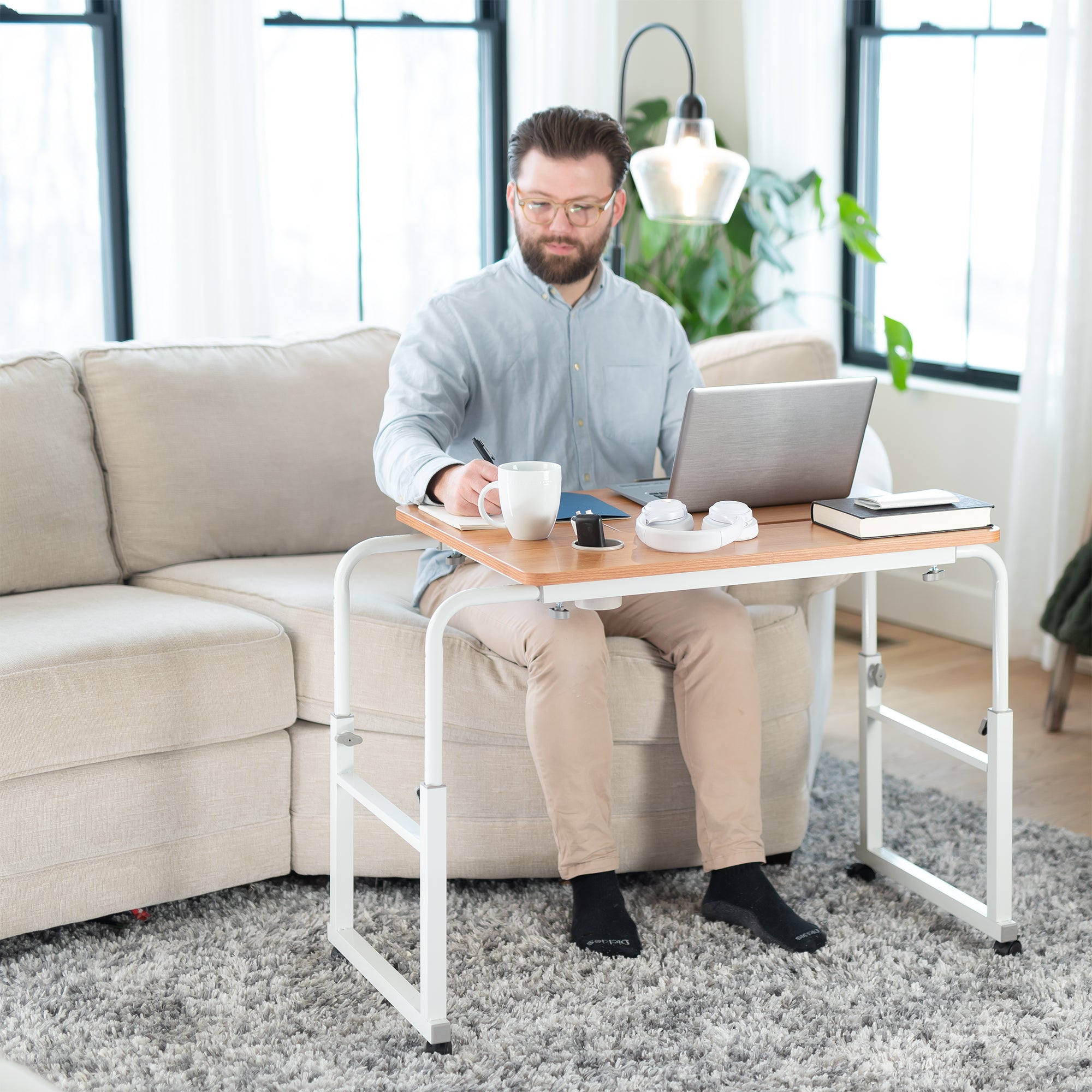 Man sitting on a couch with a laptop on a small table in a living room.