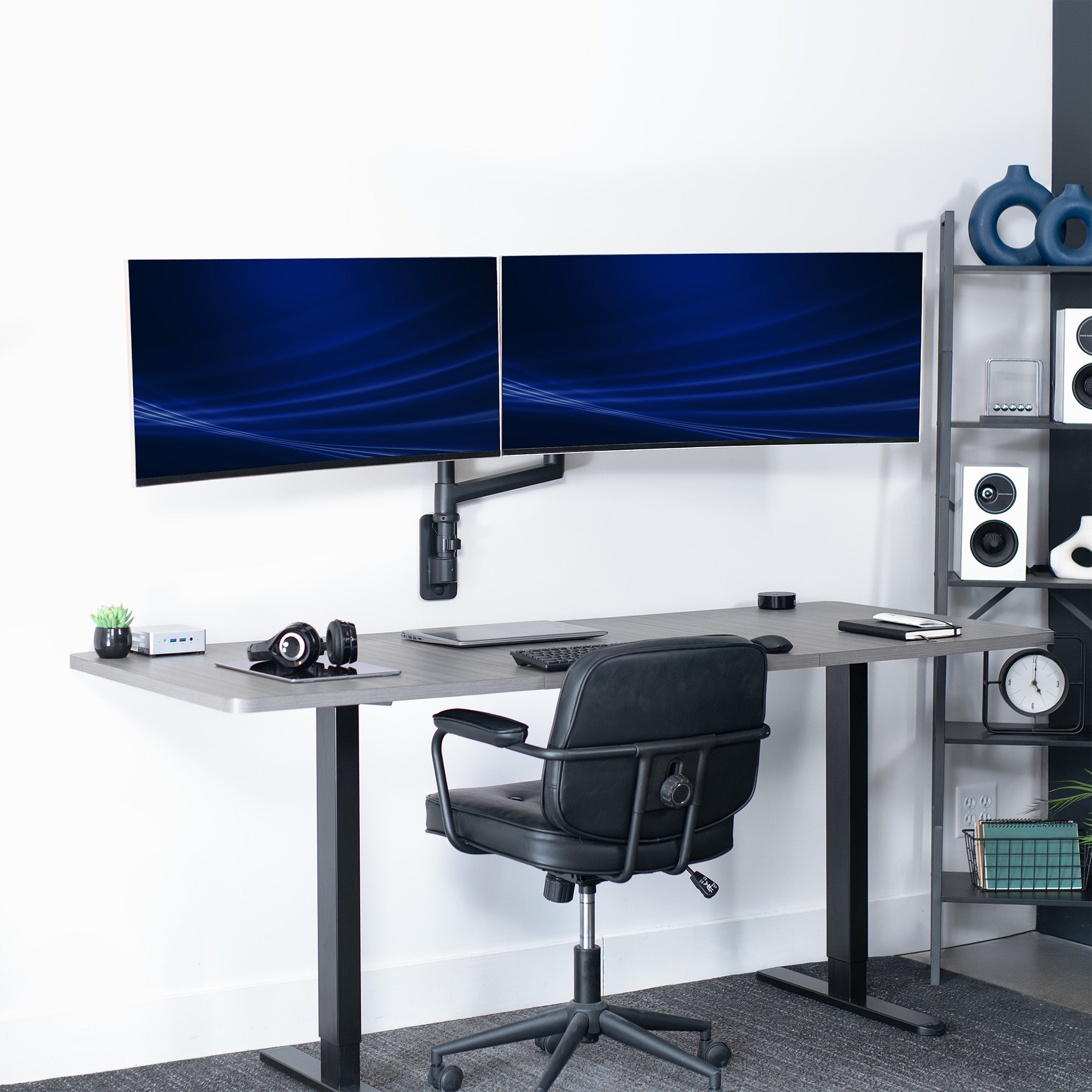 A black pneumatic arm dual ultrawide monitor wall mount holding two monitors in a home office setting.