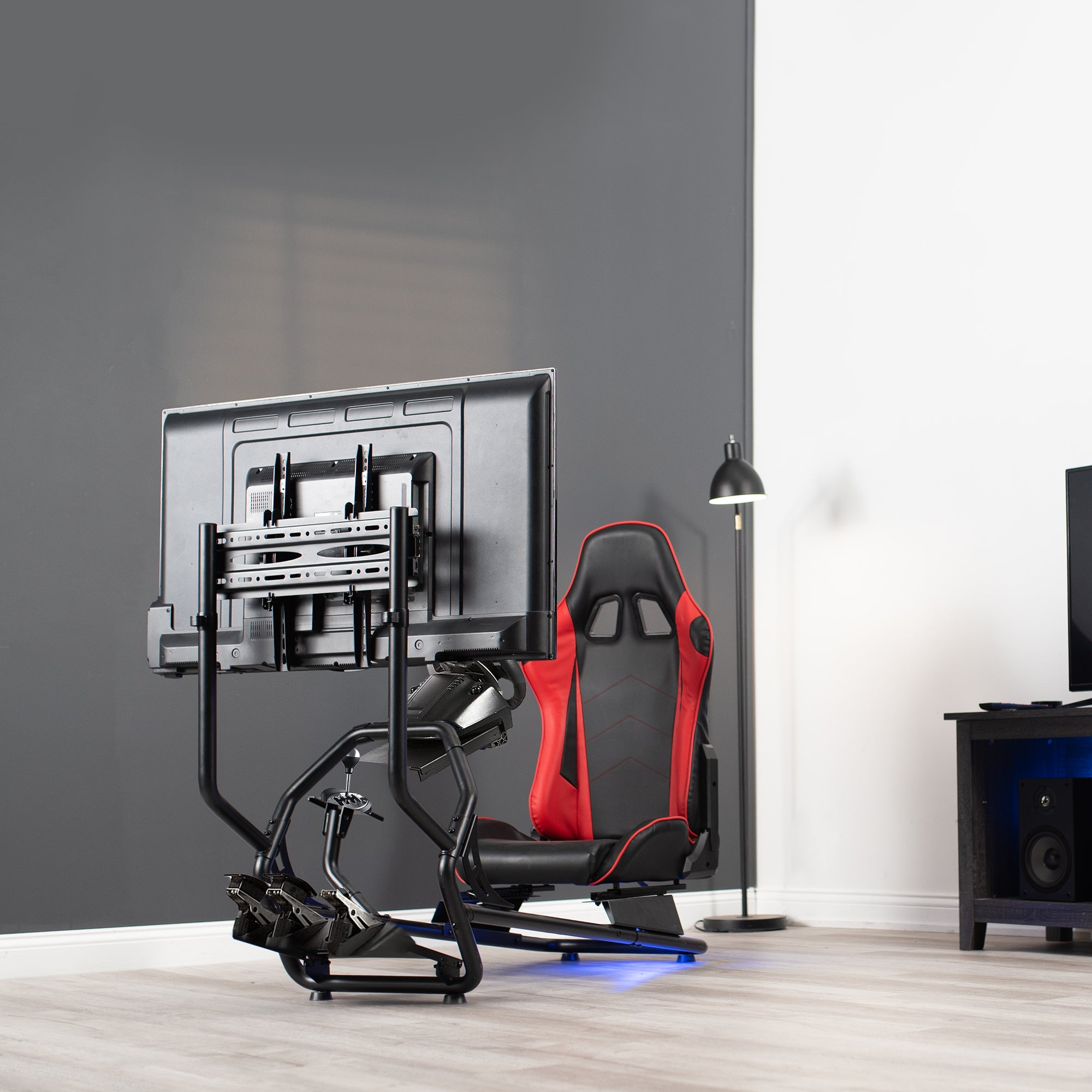 Gaming chair with red accents in a room setup with a TV and speakers.