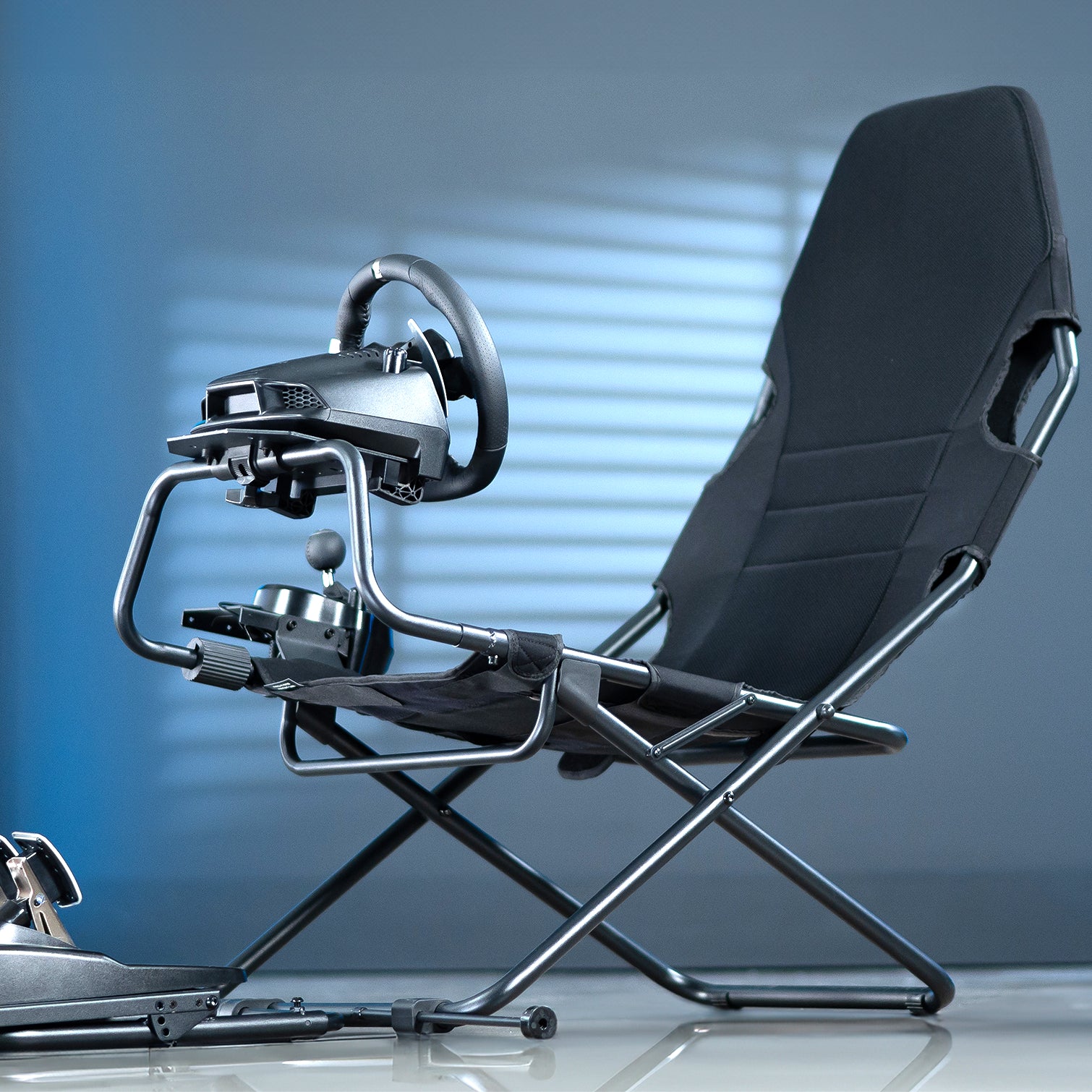 Black gaming chair with steering wheel and pedals on a reflective surface.