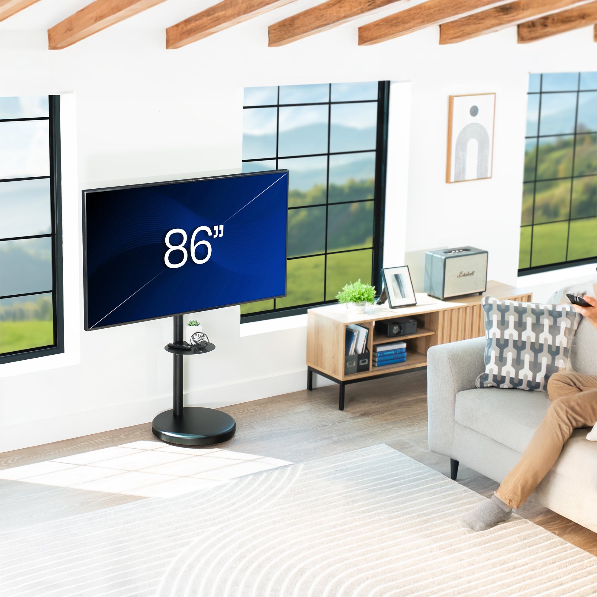 Large TV screen on TV stand displaying '86”' in a modern living room with a person sitting on a couch.