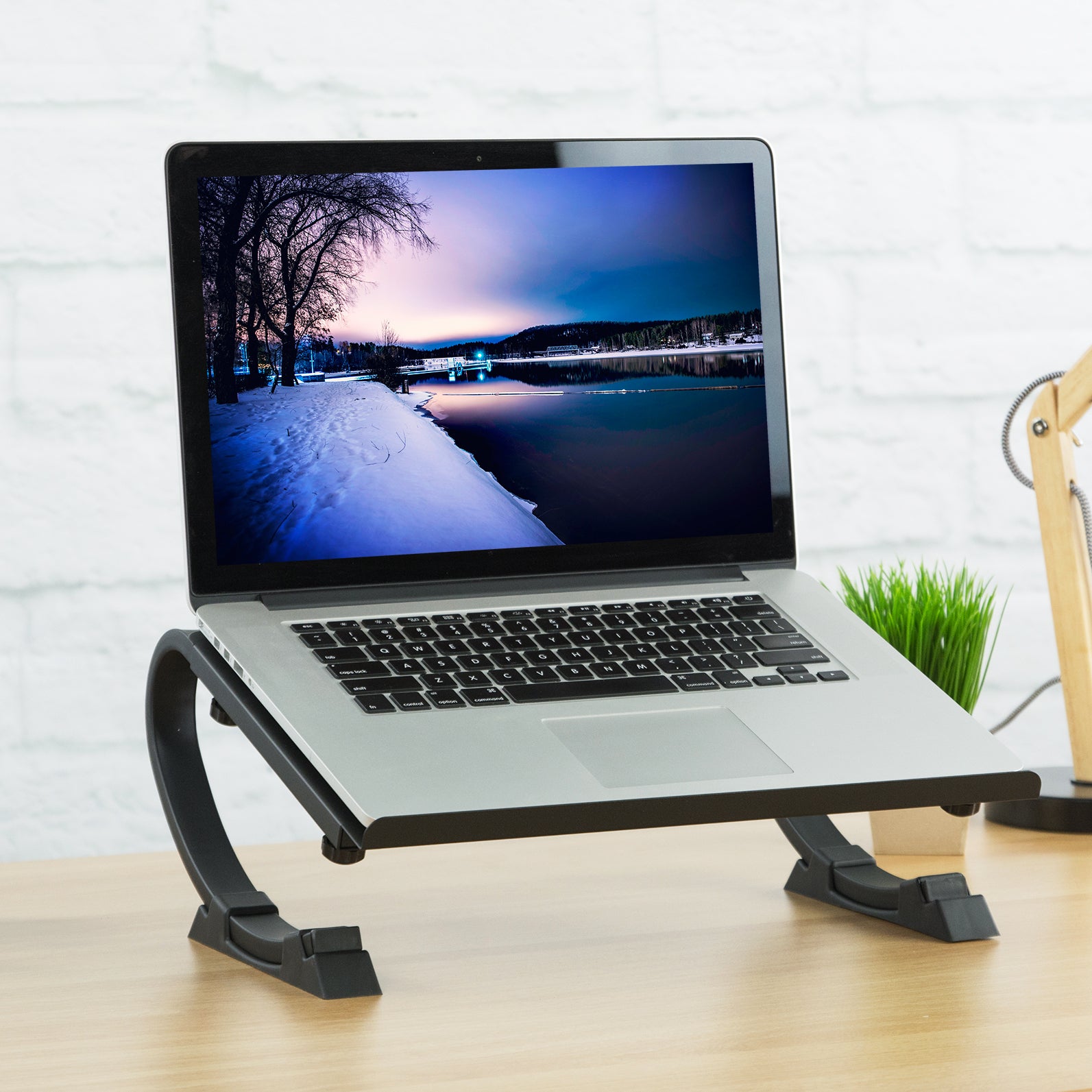 A desktop laptop stand with a plant, lamp, and other office supplies.