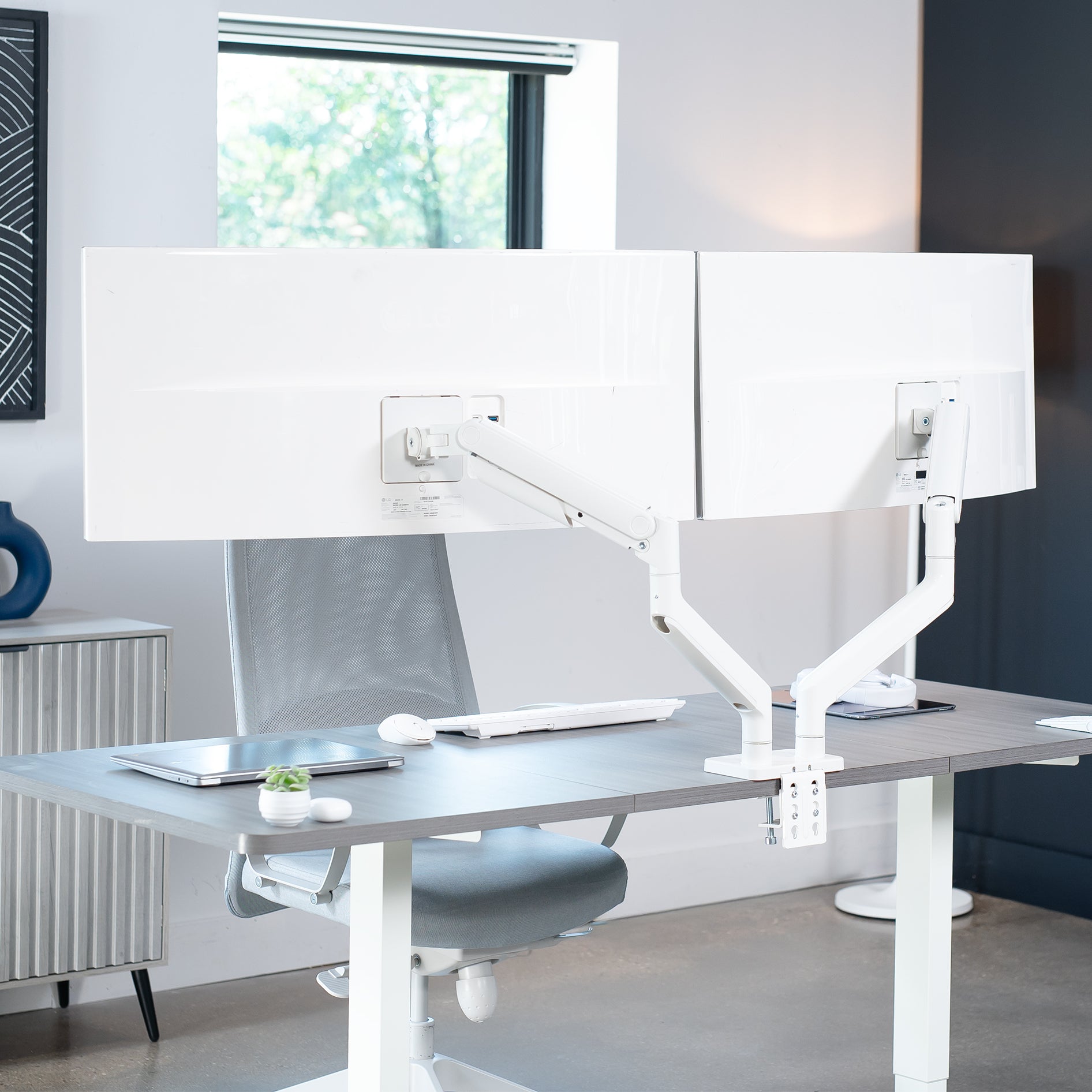 White, dual monitor desk mount with pneumatic arms, capable of supporting ultrawide screens on desk in office space.