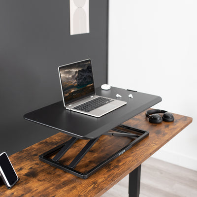 Earbuds and laptop on a desk converter for a minimalist but ergonomic setup.
