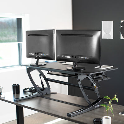 Extended desk riser with two monitors in a modern office space.
