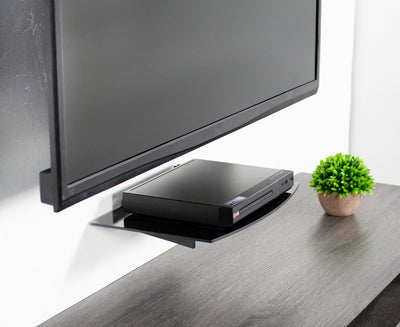 Tempered glass wall-mount shelf placed below a wall-mounted TV.