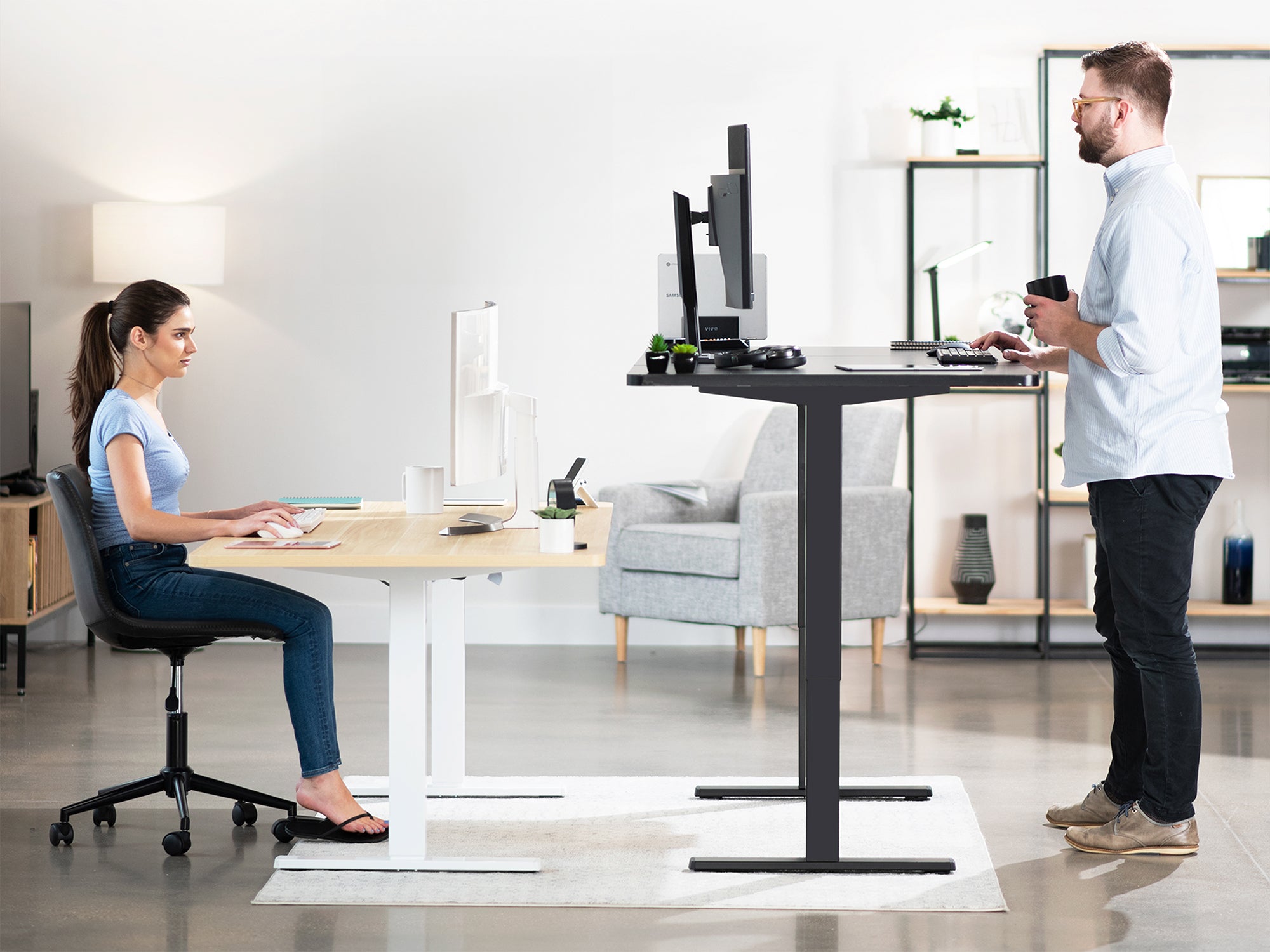 2 models in workspace, one sitting at electric desk, one standing at electric desk