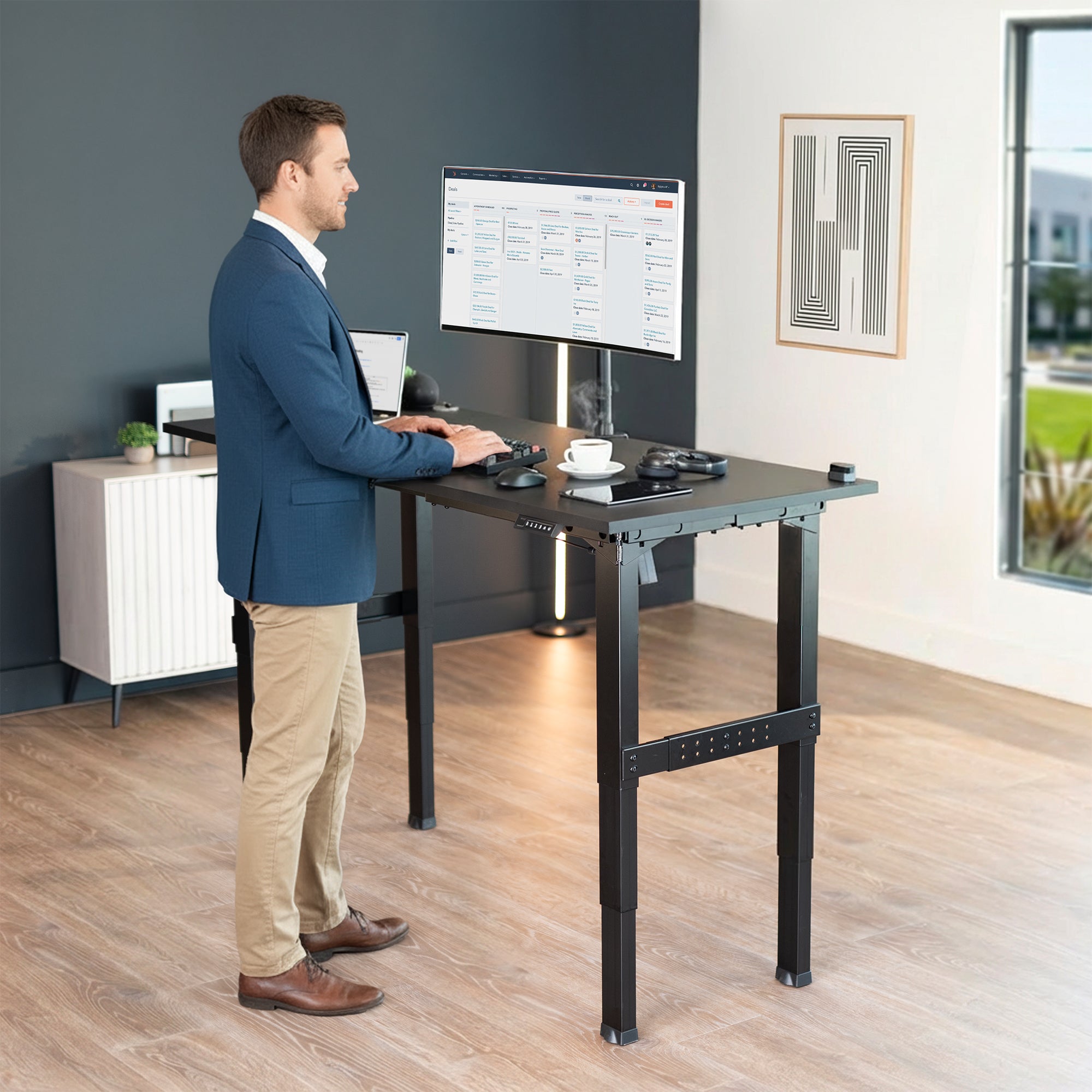 Man standing at Black Premium Electric Dual-Motor Height Adjustable 4-Leg Desk Frame with computer monitor