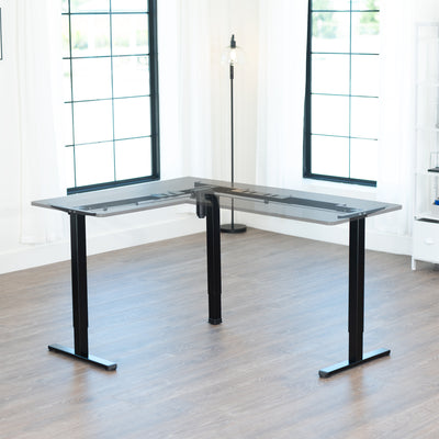 Modern L-shaped desk frame with desktop in a bright room with large windows.