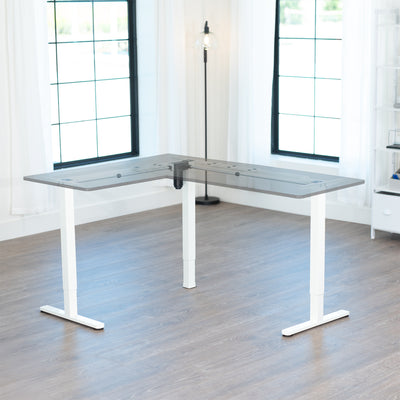 L-shaped adjustable desk frame in a room with large windows