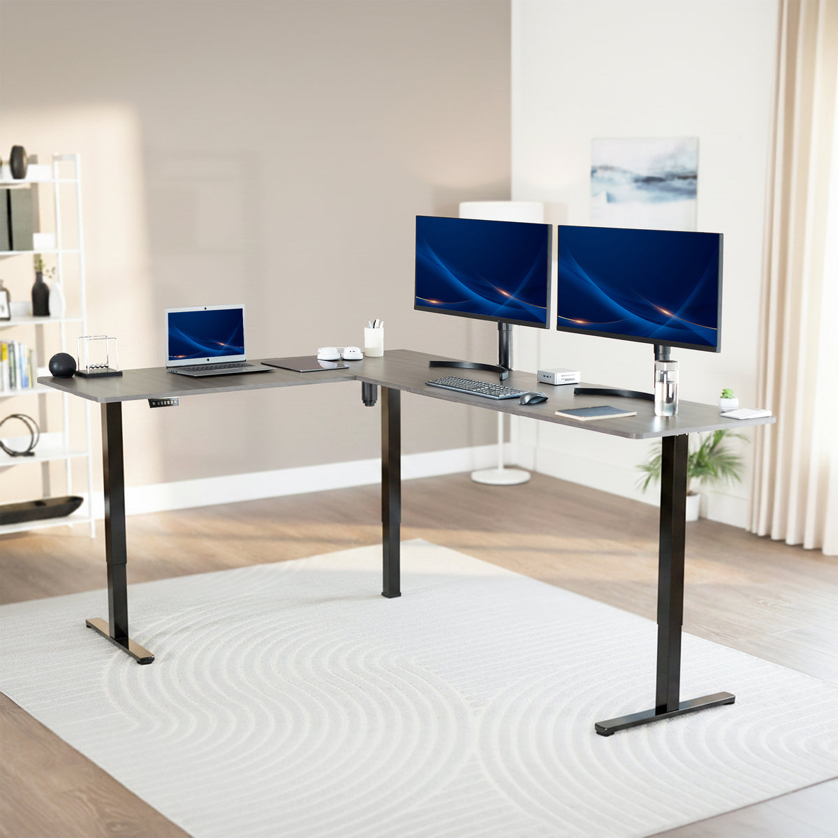 Modern office setup with a standing l-shaped desk, laptop, and two monitors in a bright room.