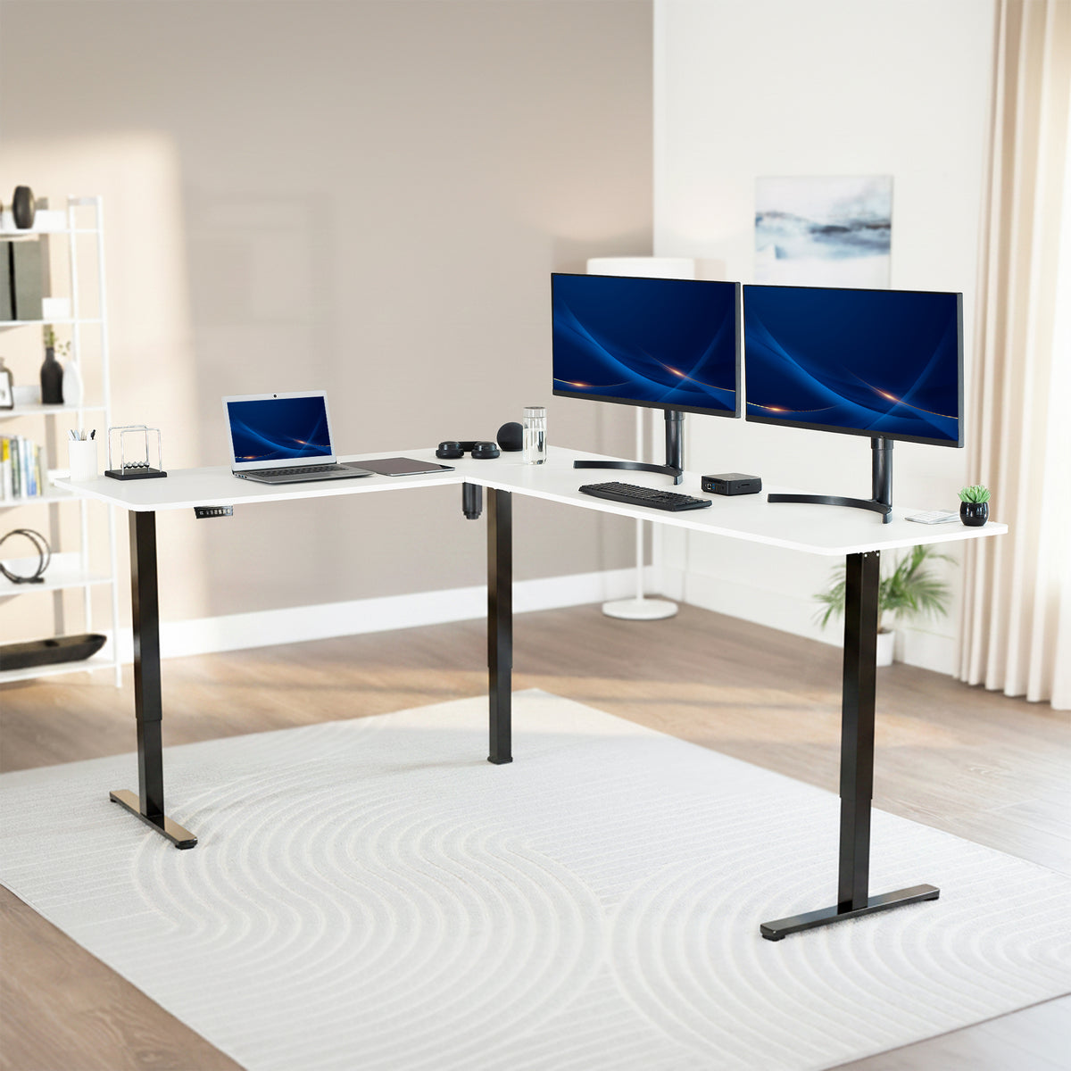 Modern office setup with a standing l-shaped desk, laptop, and two monitors in a bright room.