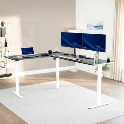 Modern office setup with a standing l-shaped desk, laptop, and two monitors in a bright room.