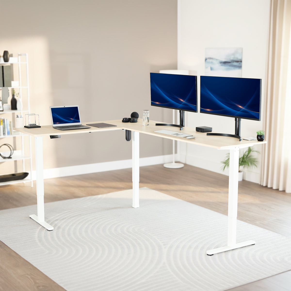 Modern office setup with a standing l-shaped desk, laptop, and two monitors in a bright room.