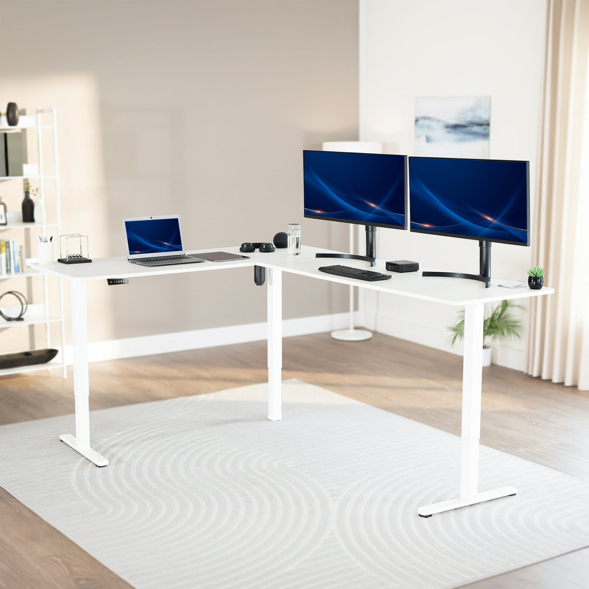 Modern office setup with a white standing l-shaped desk, laptop, and two monitors in a bright room.