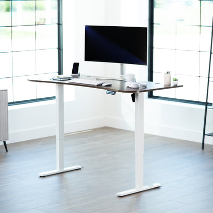 Dark walnut top white frame, electric, sit to stand, height adjustable desk in office setting.
