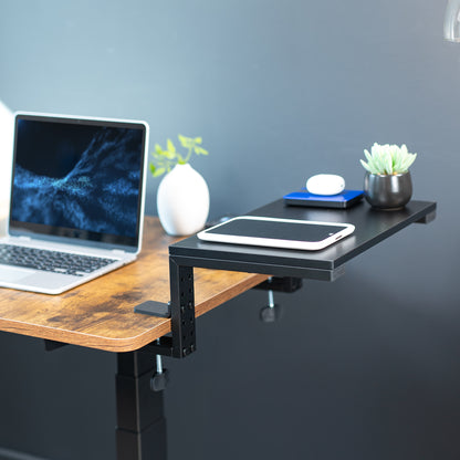Clamp-on desk extension with laptop and tablet on a wooden desk against a gray wall.
