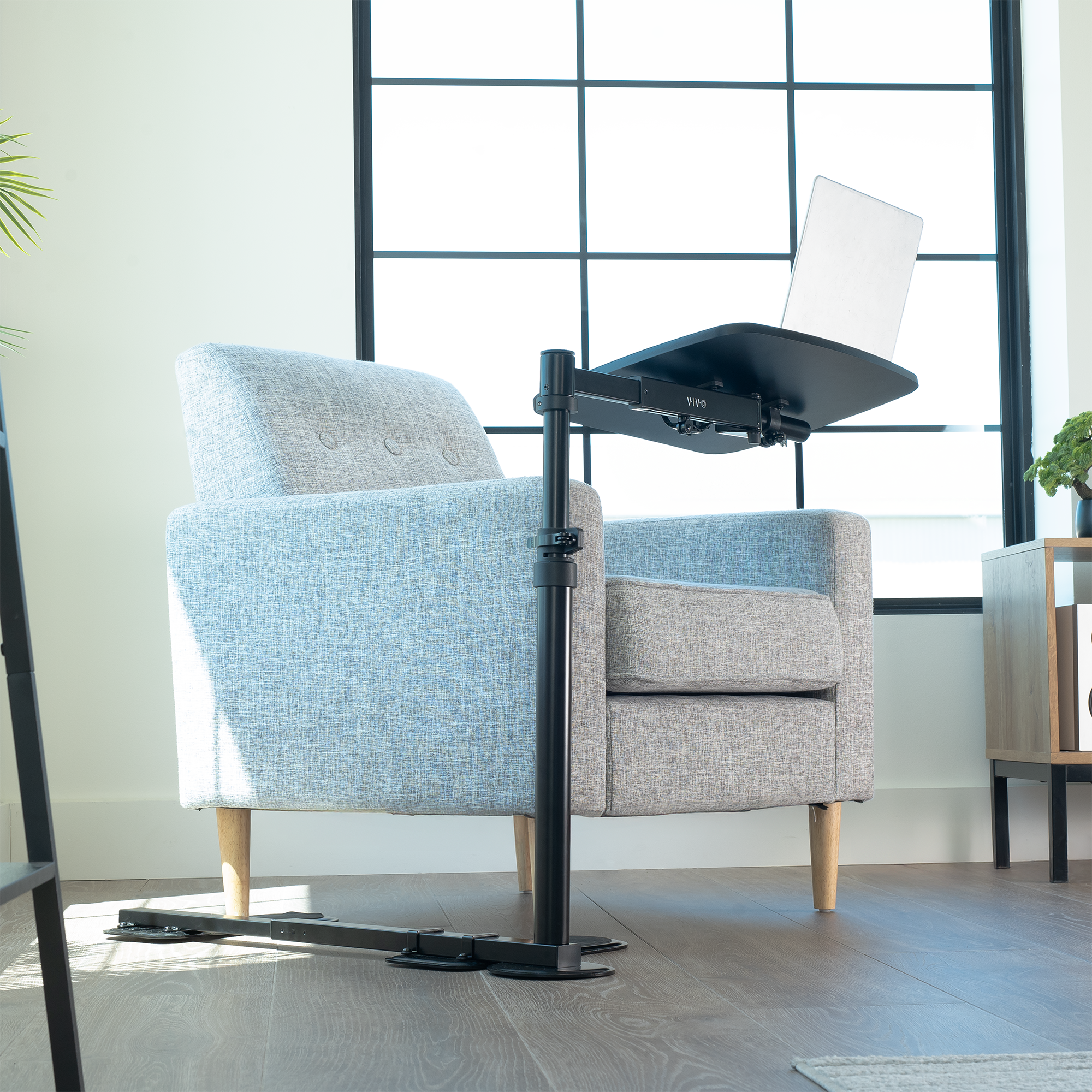 Adjustable laptop desk under a chair in a modern room with large windows.