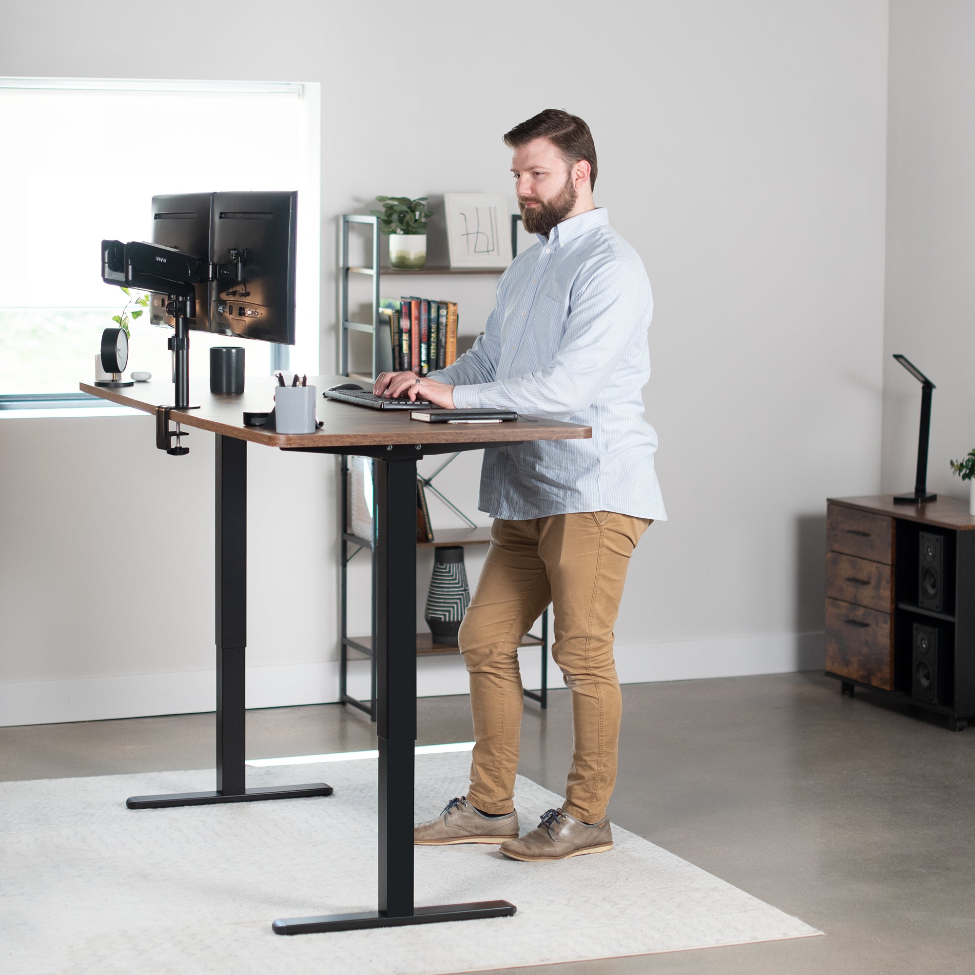 Model working at electric standing dual monitor desk in home office.