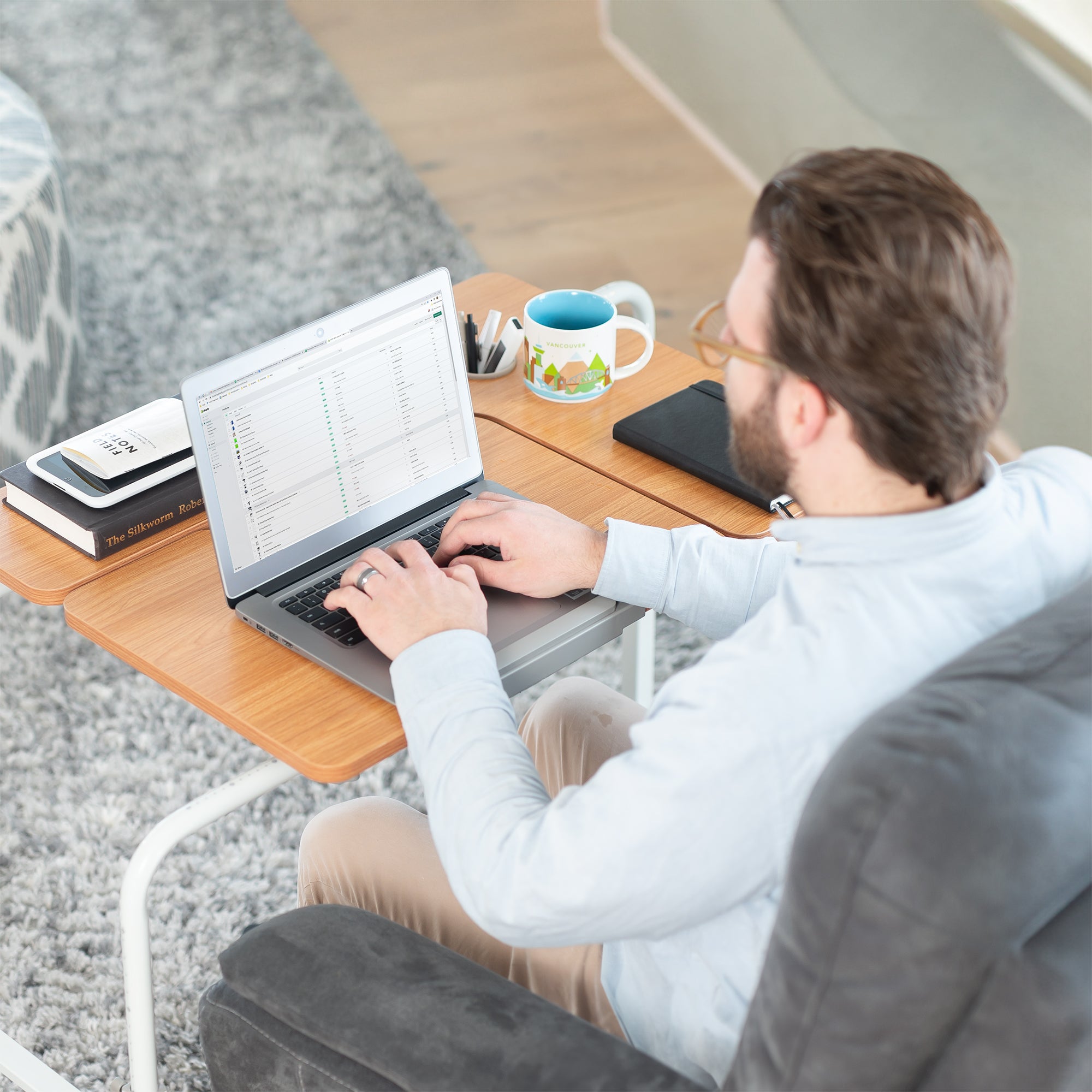 Man working on a laptop at a desk with a cup and books nearby.