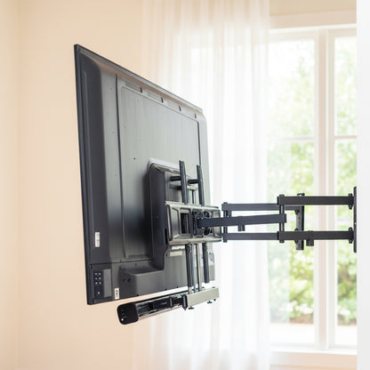TV mounted on a wall with a bracket in a room with a window featuring a  Soundbar TV Mount