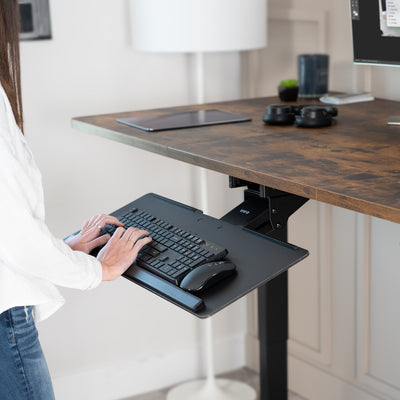 Person using a standing desk with a keyboard tray in a home office setting.