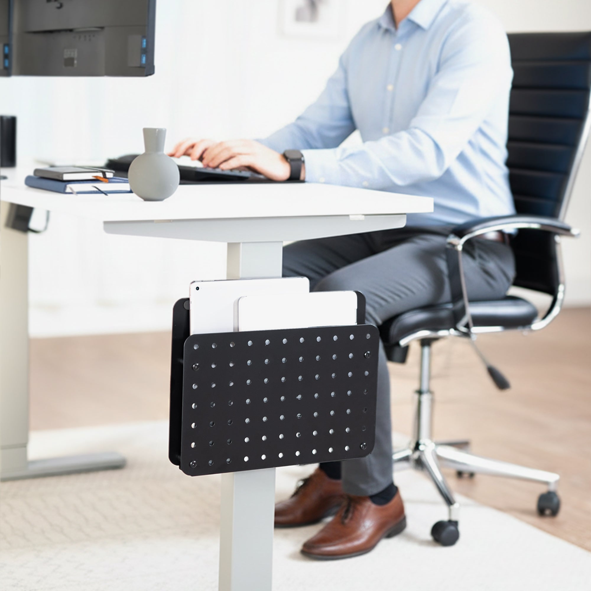 Person sitting at a desk with a black office chair and a Steel Clamp-on Desk Leg Laptop Mount Holder attached to the desk.