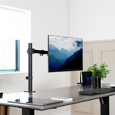 Single monitor desk mount elevating a monitor over the center of a sit-to-stand desk.