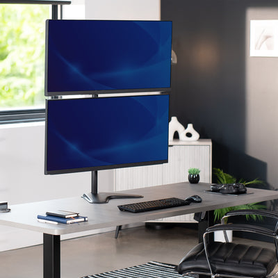 Two computer monitors on a freestanding monitor stand on a desk in an office setting with a chair and decor.