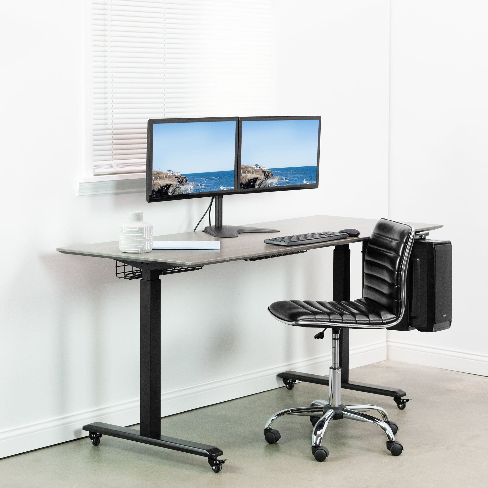 Modern office setup with a adjustable desk, dual monitors, and a black chair.