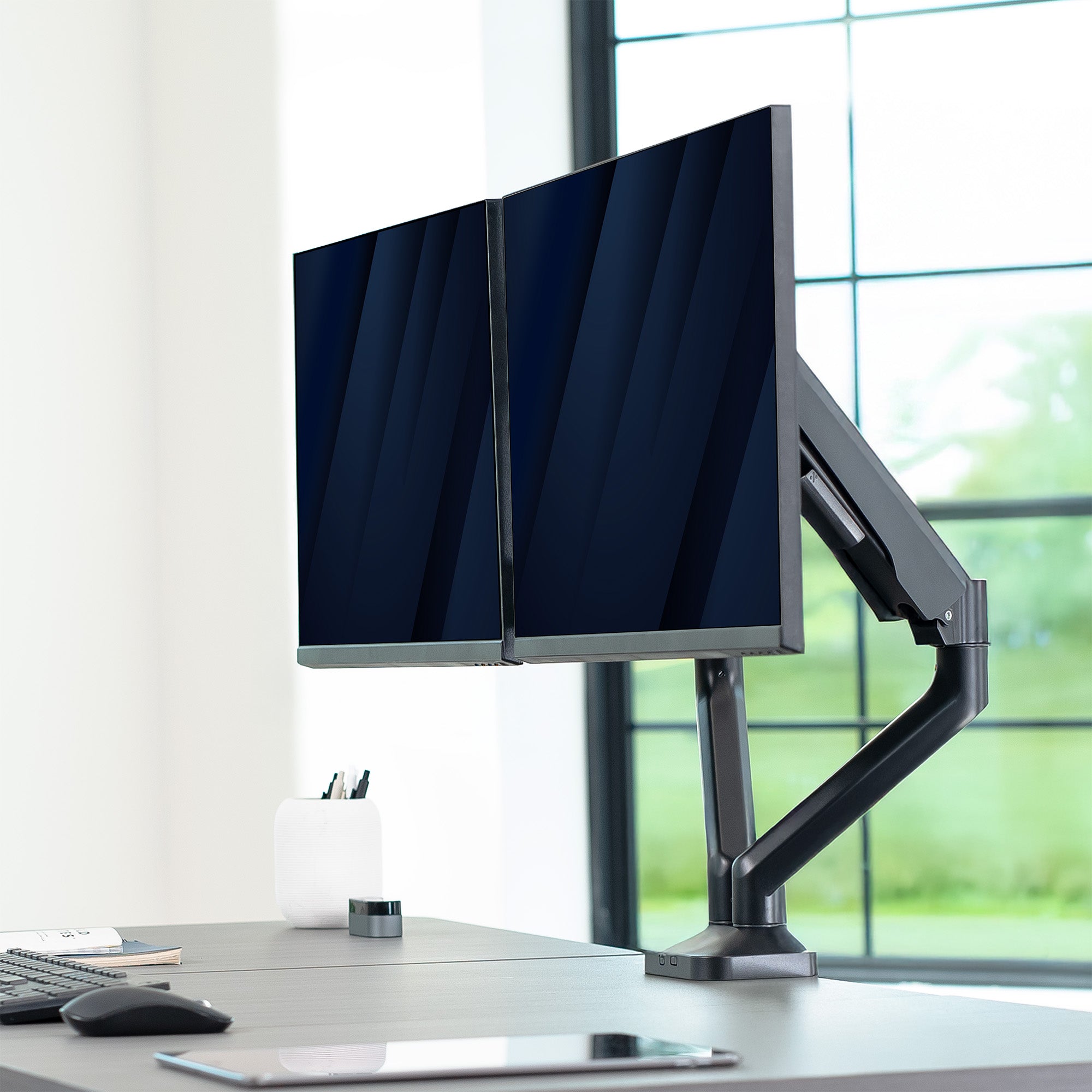 Two monitors on a desk with a flexible arm in a bright office setting