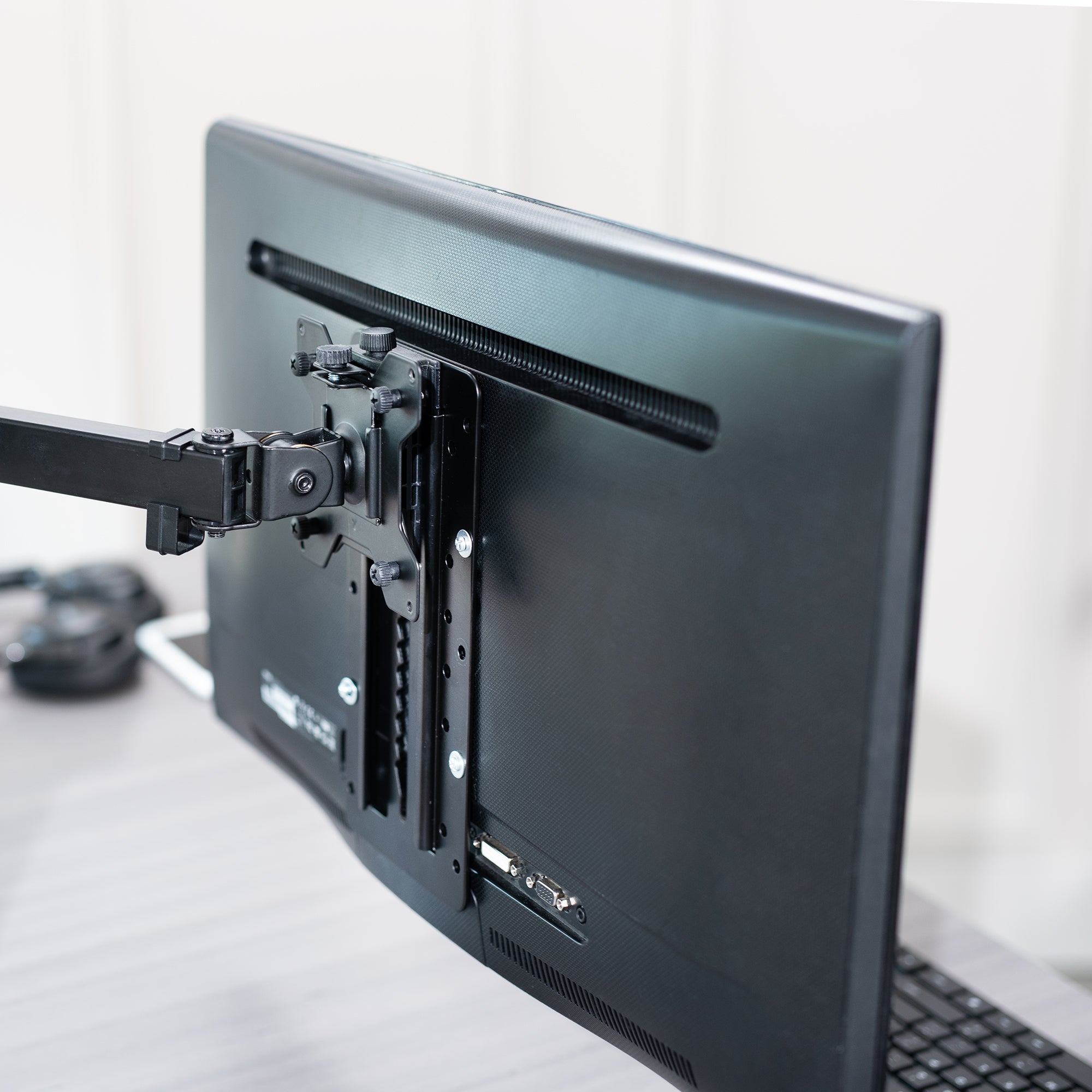 Height-adjustable Vesa adapter attached to a monitor on a desk with office background