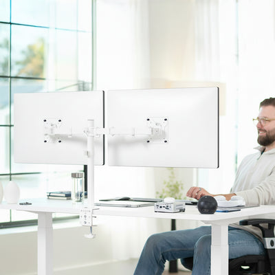 Person using a computer with dual monitors on a white desk in a bright office setting