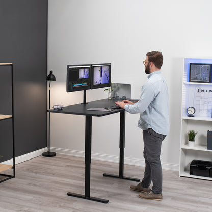 Man standing while working from a sit-to-stand hand crank height adjustable desk.