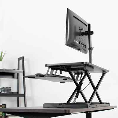 Extending black tabletop desk converter with an ergonomic monitor mount.