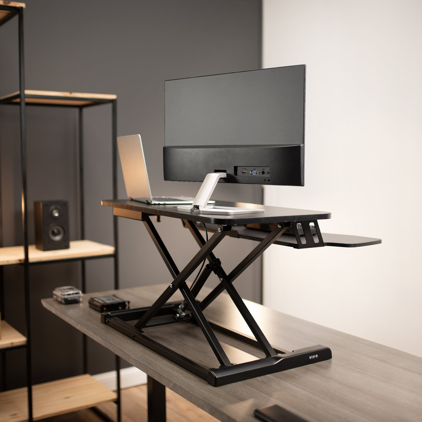 Back view of X-frame support structure of desk riser in modern office workspace elevating equipment.