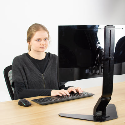 A woman working in an office from a mount monitor desk setup.