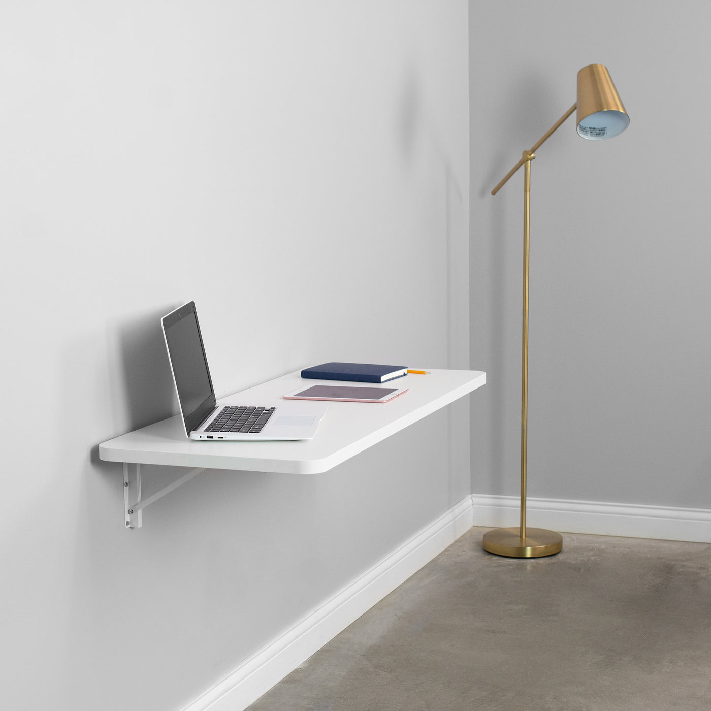 Modern and minimalist workspace with a folding shelf holding a laptop tablet and book.